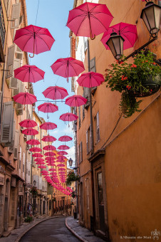 Le charme des ruelles entre balcons fleuris et parapluies rose